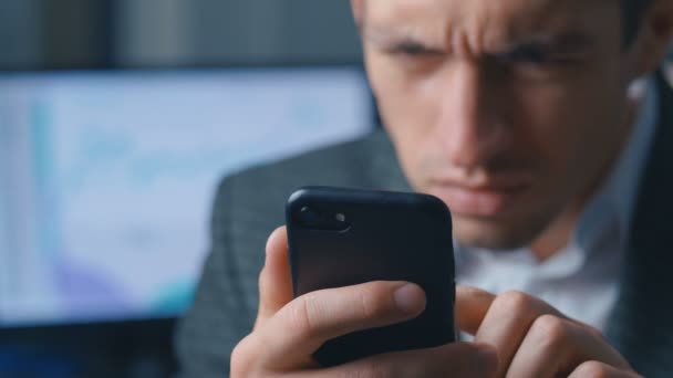 El primer plano de un hombre de negocios exitoso en un traje es el uso de un teléfono inteligente en la oficina en el lugar de trabajo. Hombre utiliza la aplicación en un teléfono móvil, oficina en el fondo — Vídeos de Stock