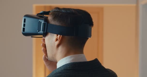 Achteraanzicht van jonge zakenman is verrast tijdens het gebruik van virtual reality bril. Man in pak krijgt ervaring met het gebruik van vr bril. — Stockvideo