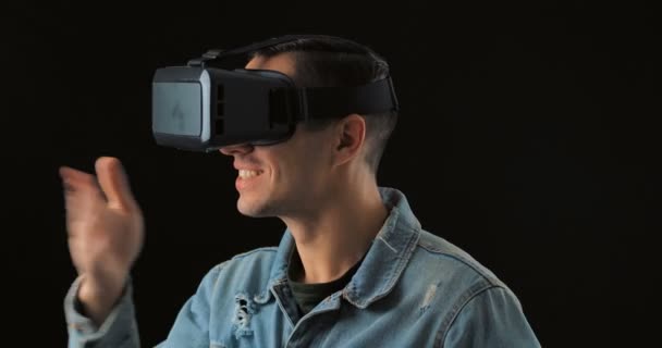 Jonge man draagt virtual reality technologie Vr Glasses. Man verrast door augmented reality in virtual reality helm op een zwarte achtergrond — Stockvideo