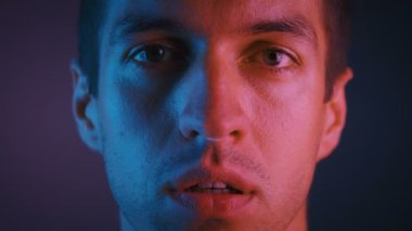 Neon ışıklar da yüzünde ciddi ve kendinden emin ifade ile kameraya bakan yakışıklı genç adamın portresi.