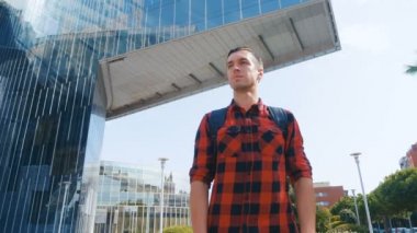 Ekose gömlekli, sırt çantalı ve sonra da kameraya bakan yakışıklı turist portresi. Büyük cam kentsel bina arka planı.