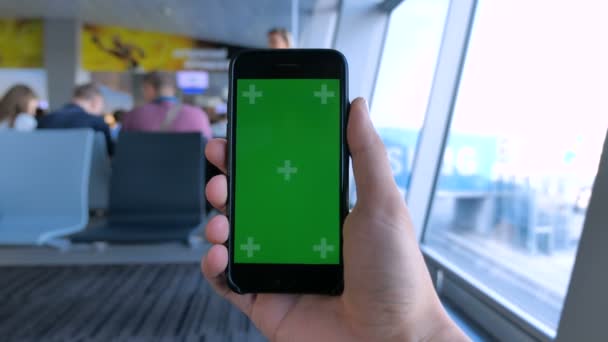 Close up man holding smartphone with green screen chroma key on at international airport background. — Stock video