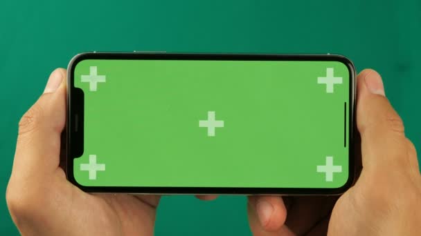 Smartphone horizontal en el primer plano de la mano aislado en fondo verde. La pantalla del teléfono es clave croma verde, fondo con otra pantalla verde croma clave. Filmación para anuncios móviles, promoción de aplicaciones . — Vídeo de stock