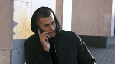 Açık şehir arka planında kabadayılıkta konuşan genç gangster uyuşturucu satıcısı portresi.