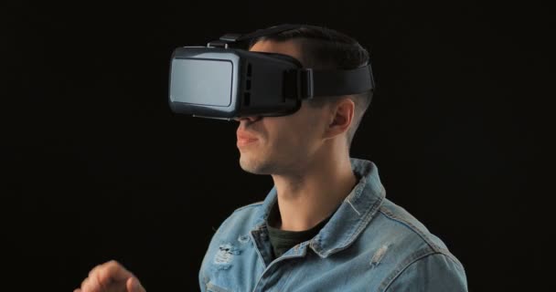 Jovem do sexo masculino usando tecnologia de realidade virtual VR Glasses. Homem surpreendido pela realidade aumentada em capacete realidade virtual em um fundo preto — Vídeo de Stock