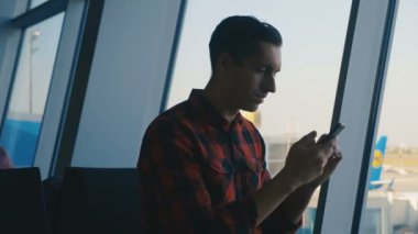 Genç bir erkek yolcu havaalanı terminalinde akıllı telefon kullanıyor.