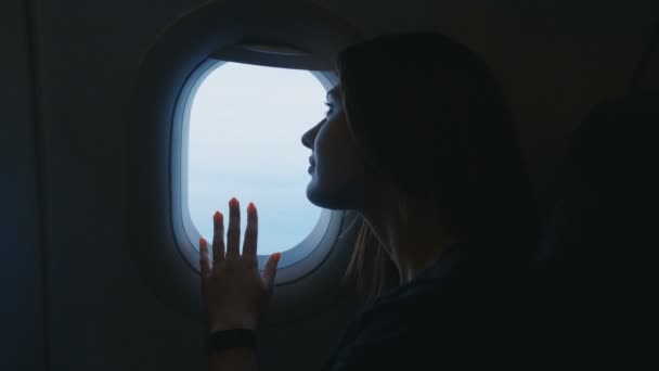 Een vrouw die met het vliegtuig reist. Jonge vrouwelijke reiziger zittend op de stoel kijkend uit een vliegtuigraam tijdens het vliegen — Stockvideo