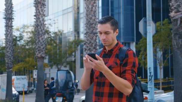 Portrait de beau jeune homme en chemise à carreaux et avec un sac à dos regardant la caméra. Grand verre fond de bâtiment urbain . — Video