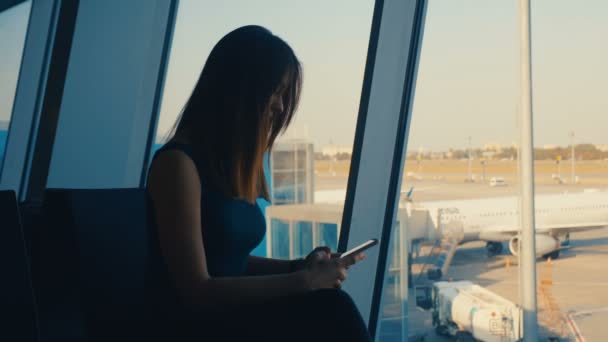 Jovem viajante usa um smartphone em um terminal de aeroporto — Vídeo de Stock