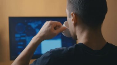 Veri merkezinde bilgisayar başında çalışan ve kahve içen insan programcı hackerın arka görüntüsü