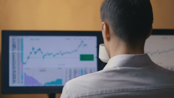 Zakenman werkt achter de computer en drinkt koffie, achteraanzicht. Mannelijke manager bekijkt stock sales statistieken in de markt. — Stockvideo