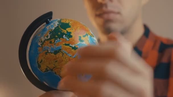 Jeune homme tenant globe. L'homme tourne un globe et le pointe du doigt. Concept de voyage . — Video