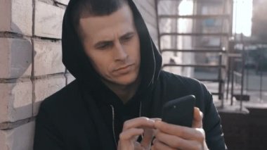 Mahalledeki genç gangster uyuşturucu satıcısı portresi açık şehir arka planında akıllı telefon kullanıyor.