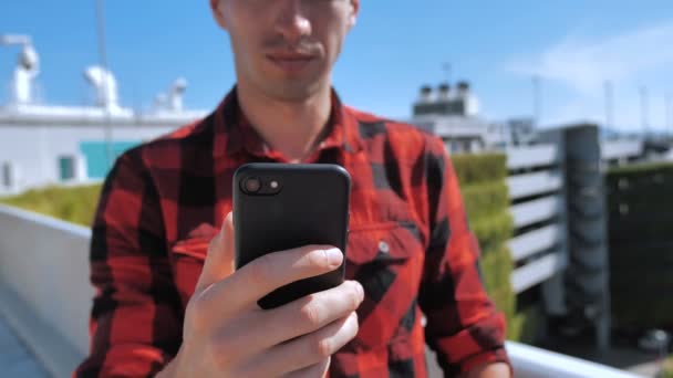 Close Up del giovane uomo attivamente scorrimento internet o social media sul suo Smartphone Fuori su edifici della città sfondo . — Video Stock