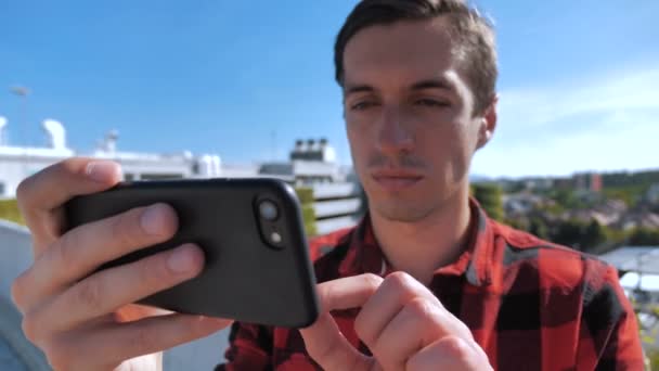 Guy watching videos on smartphone. Close up of young man watching media on his smartphone on the roof at urban area. — Stock Video