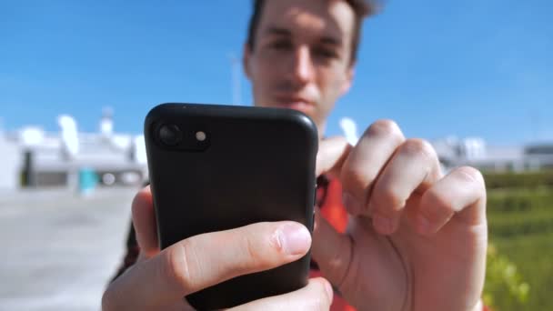 Hombre joven desplazándose por la pantalla del teléfono inteligente. Empresario usando su teléfono inteligente y pantalla móvil afuera en el techo en el fondo urbano de la ciudad — Vídeos de Stock
