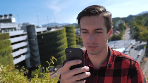 Νεαρός άνθρωπος κύλιση οθόνη smartphone. Επιχειρηματίας χρησιμοποιώντας το smartphone και την οθόνη κύλισης του έξω στην οροφή στο αστικό περιβάλλον της πόλης — Αρχείο Βίντεο