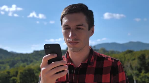 Jeune homme voyageur défilement smartphone sur beau fond de nature — Video