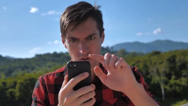 Retrato homem agressivo gritando durante o uso de telefone inteligente fora. Homem está com raiva com a mensagem que ele leu no smartphone . — Vídeo de Stock