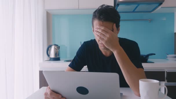 Ein depressiver junger Mann arbeitet zu Hause in der Küche an einem Laptop. Mann leidet und hat Kopfschmerzen. — Stockvideo