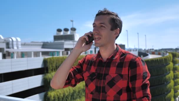 Un giovane uomo sorridente che parla al cellulare sul tetto. Ritratto di ambizioso uomo d'affari che parla di telefonia mobile all'aperto su sfondo urbano. Imprenditore discutere di affari al telefono al di fuori . — Video Stock