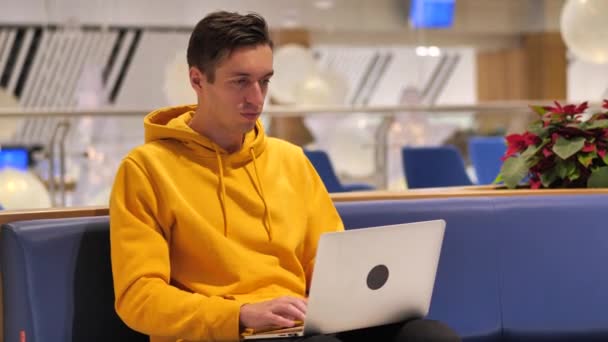 Молодий чоловік працює на ноутбуці у великому сучасному кафе — стокове відео