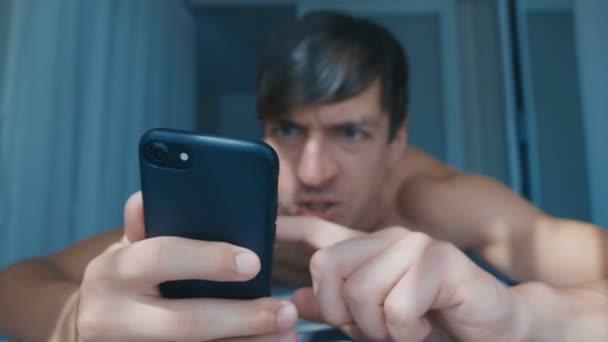 Angry Evil Naked Man reaccionando a las malas noticias en el teléfono inteligente con gritos locos mientras está acostado en la cama en casa por la mañana . — Vídeos de Stock