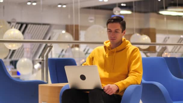 Молодий впевнений зайнятий чоловік працює на ноутбуці, сидячи в кафе — стокове відео
