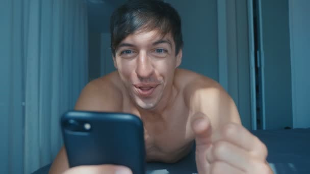 朝、自宅のベッドでスマートフォンで成功を祝う若い裸の男。勝利への感情的な反応. — ストック動画
