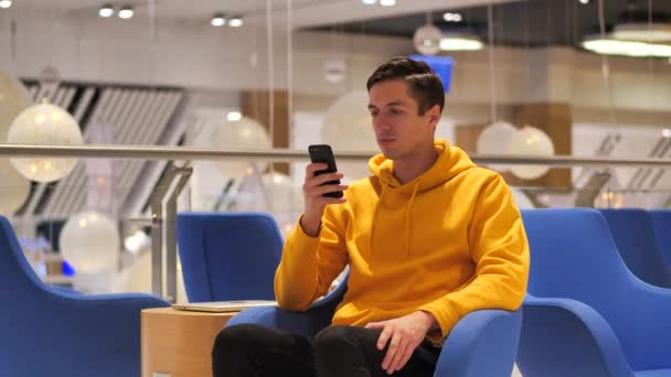 居心地の良いカフェでスマートフォンを使用して黄色のパーカーの若い男性。コミュニケーション,ビジネス,旅行,出会い系コンセプト. — ストック動画
