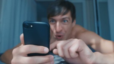 Genç Çıplak Adam Sabahları Evde Evde Yatakta Akıllı Telefon 'da Başarıyı Kutluyor. Kazanmaya Duygusal Tepki.