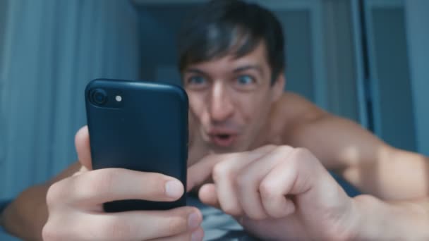 Homem nu jovem comemorando o sucesso no smartphone na cama em casa pela manhã. Reação Emocional à Vitória . — Vídeo de Stock