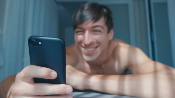 Joven hombre desnudo celebrando el éxito en el teléfono inteligente en la cama en casa por la mañana. Reacción emocional a ganar . — Vídeos de Stock