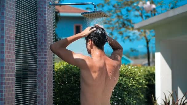 Homem atlético jovem lavando o cabelo sob a água no chuveiro ao ar livre no dia de verão em câmera lenta. Cuidado com o corpo. masculino lavagem sua cabeça sob chuveiro . — Vídeo de Stock