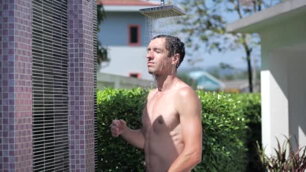 Genç atletik adam yaz günü, açık havada, duşta, suyun altında saçlarını ağır çekimde yıkıyor. Vücut bakımı. Erkek duşun altında başını yıkıyor.. — Stok video