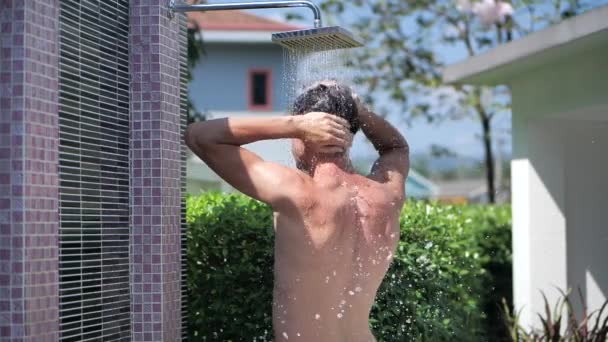 Νεαρός αθλητικός άνδρας πλένει τα μαλλιά κάτω από το νερό στο ντους σε εξωτερικούς χώρους το καλοκαίρι ημέρα σε αργή κίνηση. Φροντίδα σώματος. Άντρας πλένει το κεφάλι του στο ντους. — Αρχείο Βίντεο