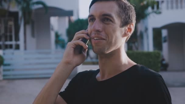 Een glimlachende man die met een smartphone praat. Portret van knappe jonge man praten door mobiele telefoon op straat. — Stockvideo
