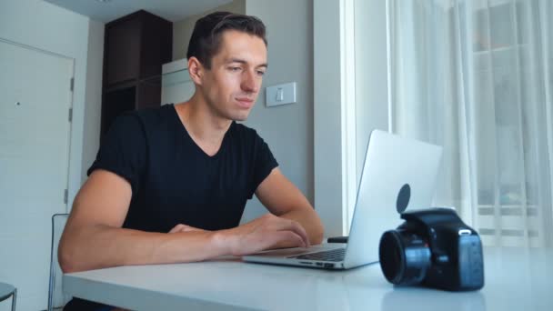Młody fotograf korzystający z laptopa przetwarzającego obrazy na laptopie i pijącego kawę w domu. — Wideo stockowe
