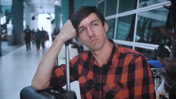 Droevige man met bagage op het vliegveld, wachtend op het instappen. Kaukasische hipster man in ruitjeshemd in terminal van vliegveld wachtend op vliegtuig — Stockvideo