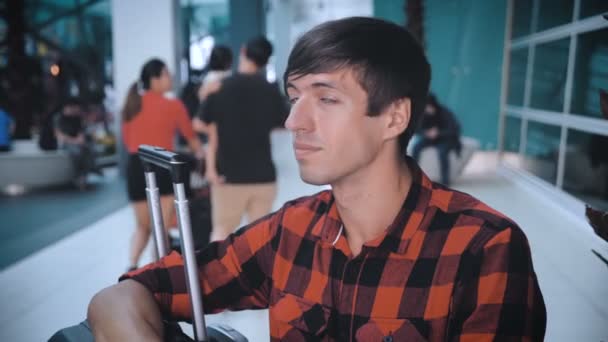 Portrait of man with bag luggage at the airport while waiting for boarding. Caucasian hipster male in plaid shirt in terminal of airport waiting for plane — Stock Video