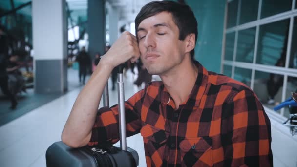 Sad man tourist with bag luggage at the airport while waiting for boarding. Caucasian hipster male in plaid shirt in terminal of airport waiting for plane — Stok video