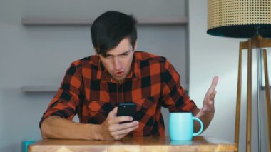 Angry Man Using Mobile phone at home. Frustrated entrepreneur is angry with the message that he read in the smartphone. Stressed businessman uses smartphone.