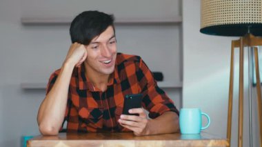 Joyful man is using smartphone having fun smiling in house alone relaxing at home