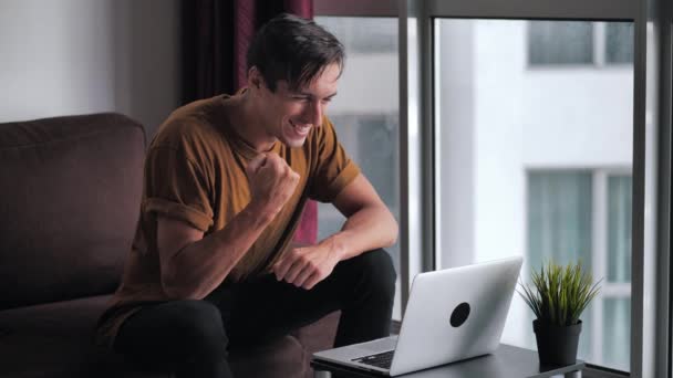 Successful Man Using Laptop Gets Surprised, then Happy and Celebrates Win While Sitting on Sofa at Home Living Room against Window — Stockvideo