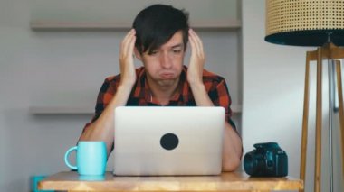 Sad man photographer crying during his work at laptop at home. Overworking concept.