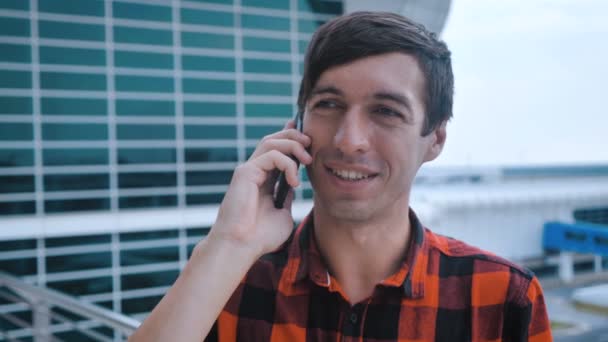 Jeune homme attrayant debout près de Big Modern Office Building. Je parle sur son Smartphone. Homme répondant à un appel téléphonique. Chemise à carreaux rouge habillée . — Video