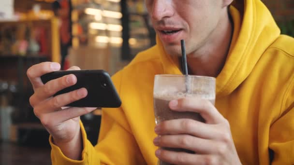 Close-up Homem usando smartphone touchscreen no café moderno. Masculino Beber batido ou smoothie e mensagens de texto no telefone inteligente no café — Vídeo de Stock