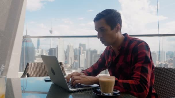 Homem bonito feliz trabalhando em um laptop celebra o sucesso Endeavor com SIM Gesto. Freelancer Trabalhando a partir de Café no fundo de arranha-céus da cidade grande . — Vídeo de Stock