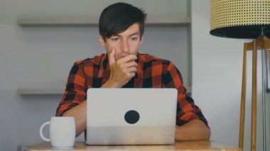 Scared man is shocked and and surprised by what he saw in the laptop while sitting at table at home