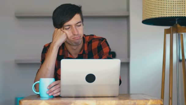 Tânăr, om de afaceri plictisit, cu laptop-ul așezat la masă acasă — Videoclip de stoc